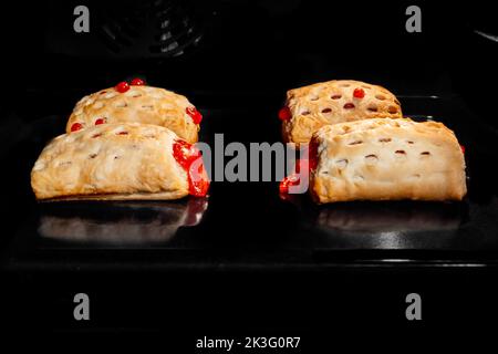 Quatre petits pains faits maison cuits à la confiture de fraises rouges dans un four électrique Banque D'Images