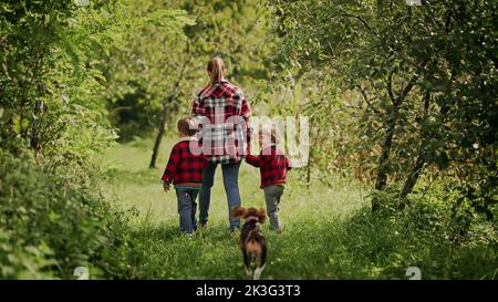 Jeune famille - maman et deux frères jumeaux garçons court avec chien beagle de chiot dans le parc ou le jardin vert. Mère et enfants heureux, amour, liberté, avenir Banque D'Images