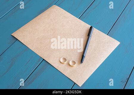 Stylo plume gris sur papier brun et à côté des anneaux de mariage. Banque D'Images