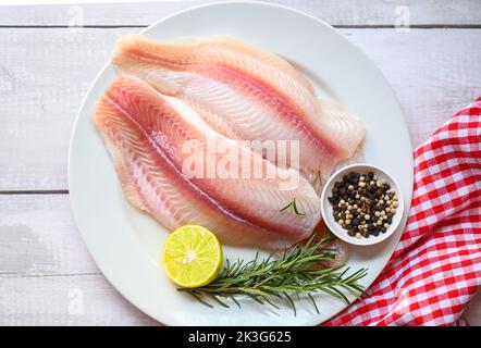 filet de poisson frais brut pangasius aux herbes et aux épices citron vert et romarin, poisson dolly de viande tilapia poisson-chat rayé, filet de poisson sur plaque blanche avec Banque D'Images