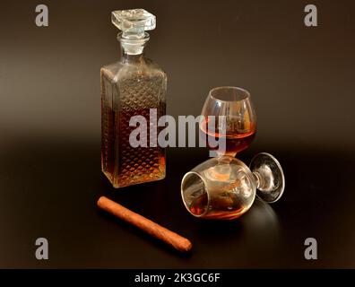 Un carafe en cristal au whisky, deux verres avec une boisson alcoolisée et un cigare cubain sur fond noir. Gros plan. Banque D'Images