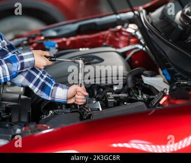 Mécanique automobile femelle en dévissant un écrou pour remplacer une bougie d'allumage de voiture. Banque D'Images