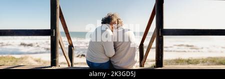 Vue panoramique d'une heureuse femme âgée souriant gaiement tout en étant assise en face de l'océan avec son mari. Un couple de personnes âgées à la retraite dépense quelque q Banque D'Images