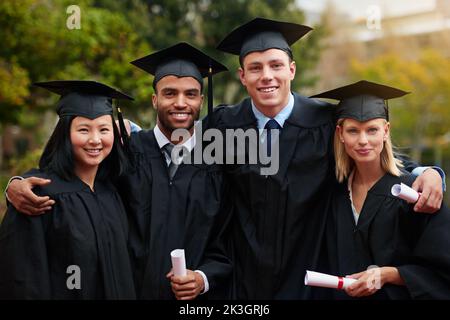 Les routes difficiles mènent souvent à de belles destinations. Un groupe de diplômés de collège debout en chapeau et en robe et portant leurs diplômes. Banque D'Images