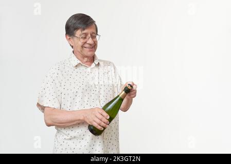 Homme hispanique senior souriant en tenant une bouteille de champagne ou de cidre et une paire de verres. Concept de toast festif. Banque D'Images