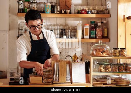 Le barista du café nettoie le comptoir et réapprovisionne les fournitures Banque D'Images