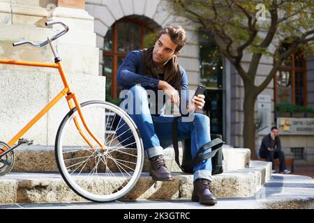 Prendre une pause bien méritée. Un jeune homme faisant une pause dans la ville avec son vélo à côté de lui. Banque D'Images