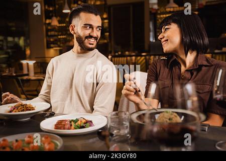Happy couple dînant au restaurant en regardant les uns les autres - couple engagé à une date prenant contact avec les yeux et manger dans la nuit dans le restaurant de luxe Banque D'Images