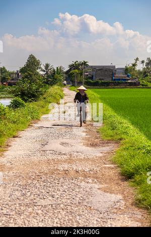 Cycliste portant un chapeau de bambou sur la route de campagne, Hai Phong rural, Vietnam Banque D'Images