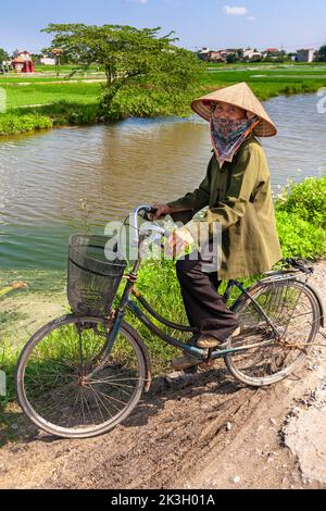 Cycliste portant un chapeau de bambou sur la route de campagne, Hai Phong rural, Vietnam Banque D'Images