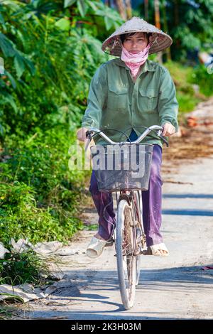 Cycliste portant un chapeau de bambou sur la route de campagne, Hai Phong rural, Vietnam Banque D'Images