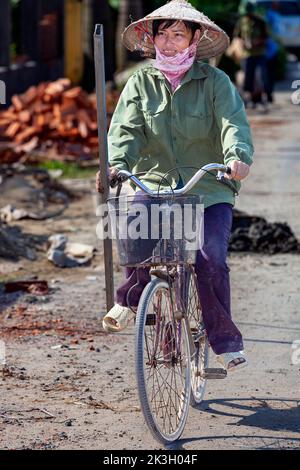 Cycliste portant un chapeau de bambou sur la route de campagne, Hai Phong rural, Vietnam Banque D'Images