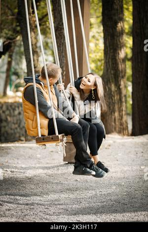 Image verticale d'un couple heureux amoureux sur une balançoire dans un parc forestier pendant la saison chaude Banque D'Images