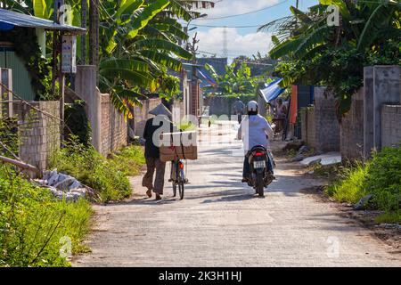 Homme vietnamien avec chapeau de bambou poussant vélo à travers le village rural de montagne Hoang Mai, Hai Phong, Vietnam Banque D'Images