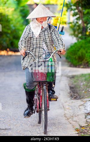 Cycliste portant un chapeau de bambou sur la route de campagne, Hai Phong rural, Vietnam Banque D'Images