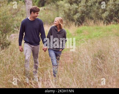 Promenade romantique dans la campagne. Un jeune couple se promenant main dans la main à travers un pré. Banque D'Images