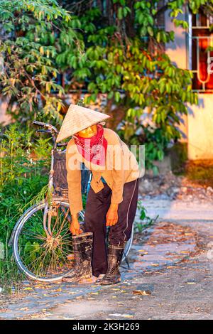 Fermier vietnamien avec vélo portant chapeau de bambou dans la campagne Hai Phong, Vietnam Banque D'Images