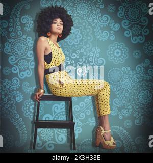 Un chic funky. Une jeune femme portant une combinaison rétro 70s tout en étant assise sur un tabouret dans le studio. Banque D'Images