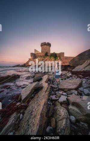 Fort de Socoa avec une femme se tenant sur la plage de forme de flysch unique au coucher du soleil à Ciboure et Saint-Jean-de-Luz Banque D'Images