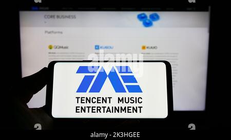 Personne tenant un smartphone avec le logo de la société Tencent Music Entertainment Group à l'écran devant le site Web. Mise au point sur l'affichage du téléphone. Banque D'Images