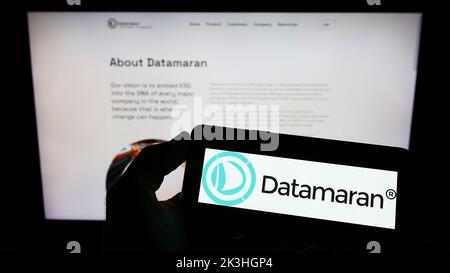 Personne tenant un téléphone portable avec le logo de la société britannique de logiciels ESG Datamaran Ltd. À l'écran devant la page Web. Mise au point sur l'affichage du téléphone. Banque D'Images