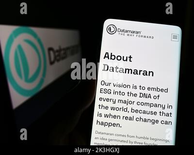 Personne tenant un téléphone portable avec la page Web de la société britannique de logiciels ESG Datamaran Ltd. À l'écran devant le logo. Concentrez-vous sur le centre de l'écran du téléphone. Banque D'Images