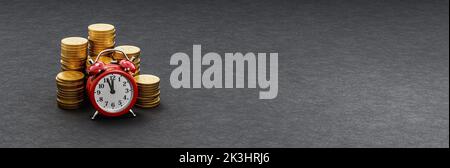 Réveil devant des piles de pièces sur fond sombre Banque D'Images