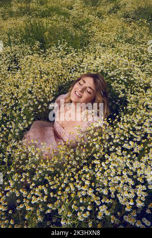 Jeune femme blonde portant une robe rose bouffée dans un champ de fleurs en été Banque D'Images