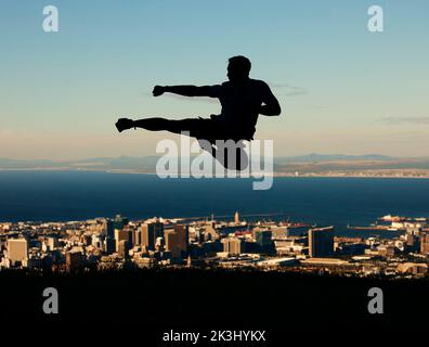 Silhouette de l'homme faisant le karaté avec le ciel et la ville en arrière-plan. Aperçu de l'athlète masculin qui frappe et frappe dans l'air dans le mouvement des arts martiaux Banque D'Images