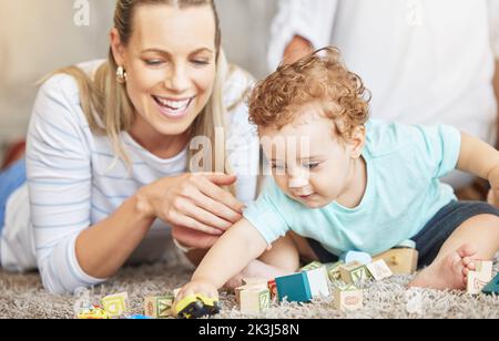 La mère, l'enfant et le jeu bloc d'apprentissage jouets sur le sol pour le collage éducatif temps ensemble dans la maison de famille. Jeune femme, bienveillante et aimante aidant le tout-petit Banque D'Images