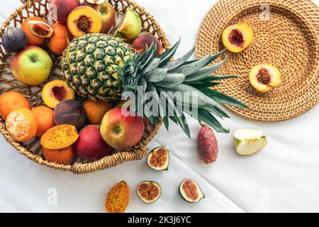Ananas et autres fruits exotiques dans un panier en osier sur fond blanc. Banque D'Images