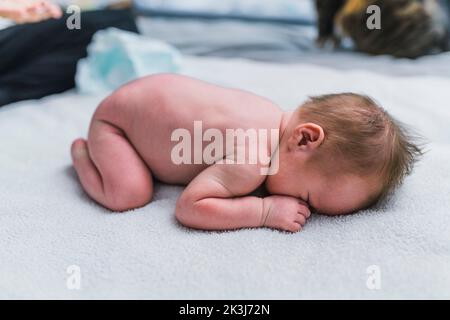 Nouveau-né garçon avec des cheveux bruns qui se posent sur son ventre dans une position foetale et se cachant son visage pendant le changement d'une couche. Photo de haute qualité Banque D'Images