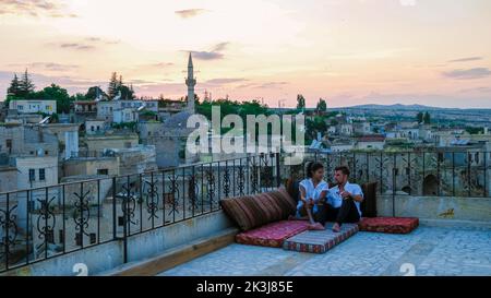 Couple heureux avec un verre sur le toit d'une maison de grotte village historique d'Ayvalii Goreme Cappadocia, couple regarder le coucher du soleil Kapadokya. Banque D'Images