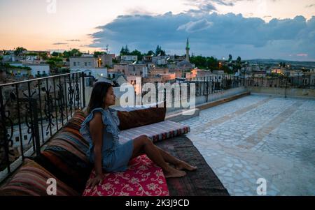 Couple heureux avec un verre sur le toit d'une maison de grotte village historique d'Ayvalii Goreme Cappadocia, couple regarder le coucher du soleil Kapadokya. Banque D'Images