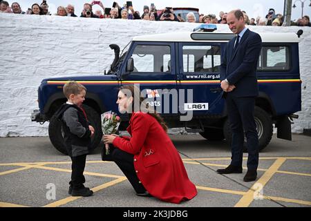 Le prince de Galles (à droite) regarde sa femme la princesse de Galles reçoit une belle fleur de Theo Crompton, quatre ans, lors de sa visite à la station de sauvetage RNLI Hollyhead à Anglesey, dans le nord du pays de Galles, où ils ont rencontré l'équipage, bénévoles et certains de ceux qui ont été soutenus par leur unité locale. Date de la photo: Mardi 27 septembre 2022. Banque D'Images