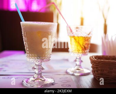 Deux verres avec boissons dans un restaurant, un cocktail de noix de coco avec une paille et du jus de pomme sur fond de lumière de fenêtre. Boissons d'été, boissons Banque D'Images