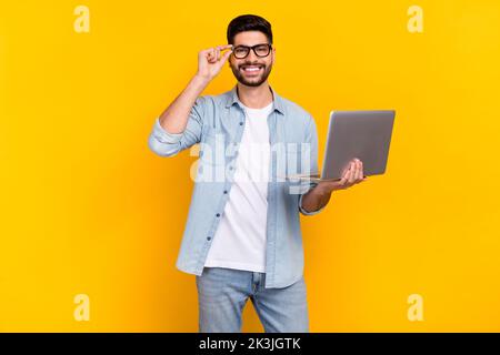 Photo de gai latin jeune gars toucher lunettes visite travail à distance conférence porter élégant Jean look isolé sur fond jaune Banque D'Images