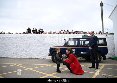 Le prince de Galles (à droite) regarde sa femme la princesse de Galles reçoit une belle fleur de Theo Crompton, quatre ans, lors de sa visite à la station de sauvetage RNLI Hollyhead à Anglesey, dans le nord du pays de Galles, où ils ont rencontré l'équipage, bénévoles et certains de ceux qui ont été soutenus par leur unité locale. Date de la photo: Mardi 27 septembre 2022. Banque D'Images