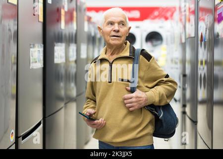 homme âgé à la recherche d'un réfrigérateur au comptoir dans la salle d'exposition du service d'hypermarché des appareils électriques Banque D'Images