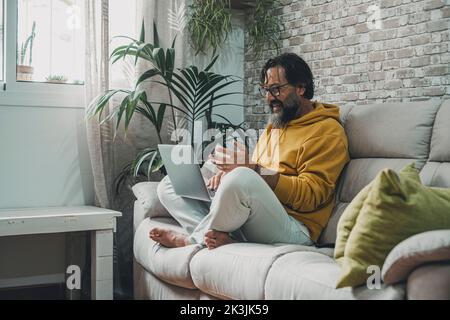 Homme mature à la maison assis sur le canapé pour passer des appels vidéo avec un ordinateur portable. Des hommes heureux et modernes travaillent sur un ordinateur portable et une connexion Internet sans fil. S Banque D'Images