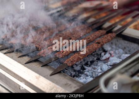 Les kebabs traditionnels d'Adana grillent sur un barbecue, gros plan, fumée Banque D'Images