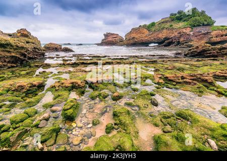 Vue panoramique sur le rivage avec des rochers et des eaux peu profondes à Biarritz, France contre un ciel de tempête spectaculaire Banque D'Images