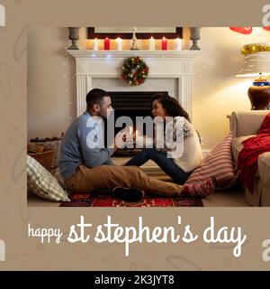 Composition du texte du jour de St stephen et couple biracial à noël par cheminée Banque D'Images