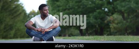 Le jeune homme en t-shirt blanc regarde autour assis sur l'asphalte Banque D'Images