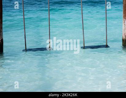 Deux balançoires vides sur l'eau au bord de la mer sur une plage tropicale. Concept de voyage de vacances Banque D'Images