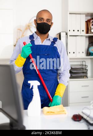 Nettoyant masculin dans un masque de protection et uniforme au bureau Banque D'Images