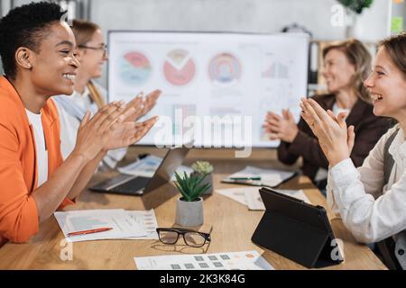 Gros plan sur les femmes multiraciales qui se clachent entre les mains tout en étant assis ensemble au bureau. Concentrez-vous sur les tablettes et PC portables modernes. Réunion d'affaires réussie. Banque D'Images