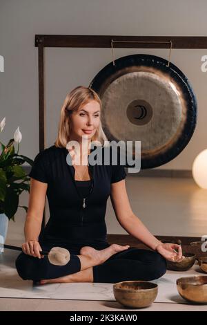 Une femme est assise avec un marteau et à côté d'un gong et de bols tibétains à l'intérieur. Banque D'Images