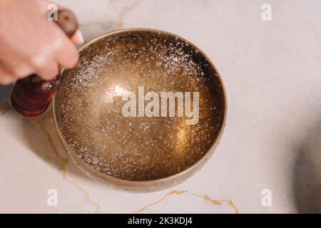 Gros plan de la main d'une femme jouant sur un bol tibétain rempli d'eau. Banque D'Images