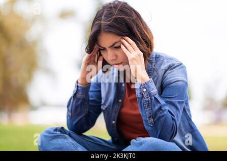 Concept de dépression. Bouleverser la femme arabe assise à l'extérieur et se touchant la tête dans le désespoir Banque D'Images
